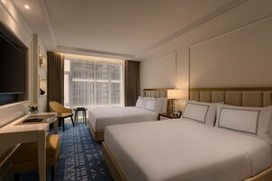 Habitación de hotel con dos camas, un escritorio, una silla, un televisor y una ventana con cortinas.