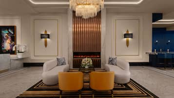 A modern lobby with a chandelier, two sofas, a fireplace, and a reception desk.
