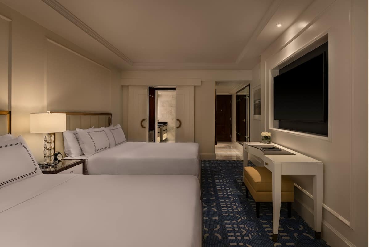 A hotel room with two beds, a desk, a TV, and a bathroom visible through an open door.