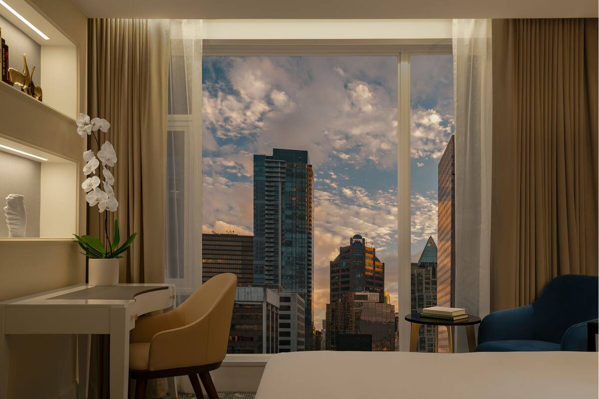 A hotel room with a large window, a desk, a chair, and a blue armchair.