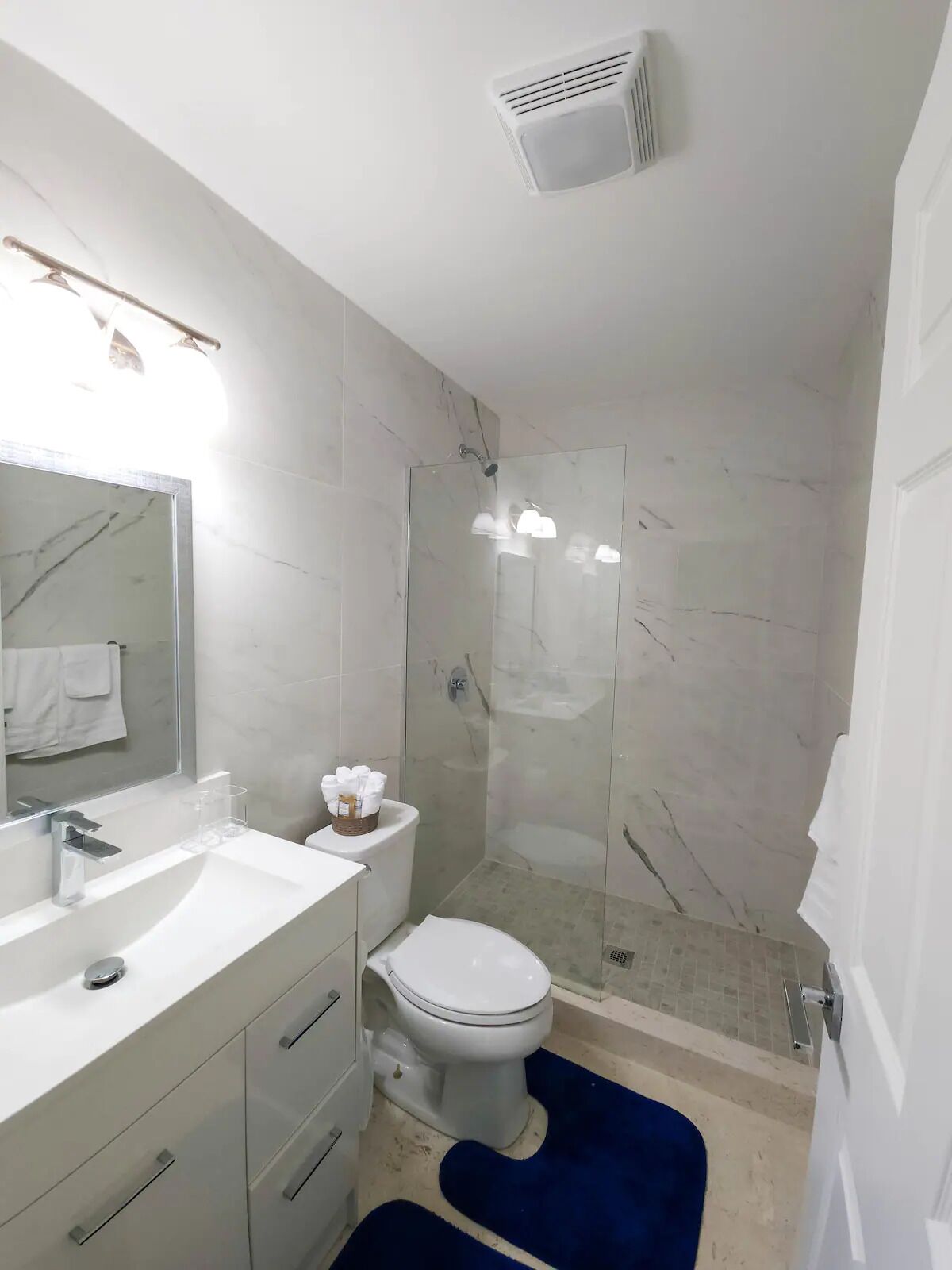 Une salle de bain moderne avec un lavabo blanc, un miroir et des toilettes, une douche en verre et un mur recouvert de carreaux de marbre.
