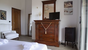 A hotel room with a wooden dresser, a television, a bed with white linens, and artwork on the walls. - Villa Lina.Independent, with swimming pool and view of the Aeolian islands (Caronia)