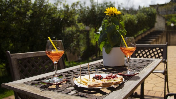 A wooden table with a plate of food and two drinks, surrounded by greenery and a bench. - Villa Lina.Independent, with swimming pool and view of the Aeolian islands (Caronia)