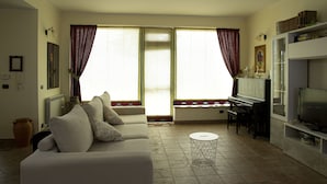 A living room with a sofa, a piano, a television, and a window with curtains. - Villa Lina.Independent, with swimming pool and view of the Aeolian islands (Caronia)