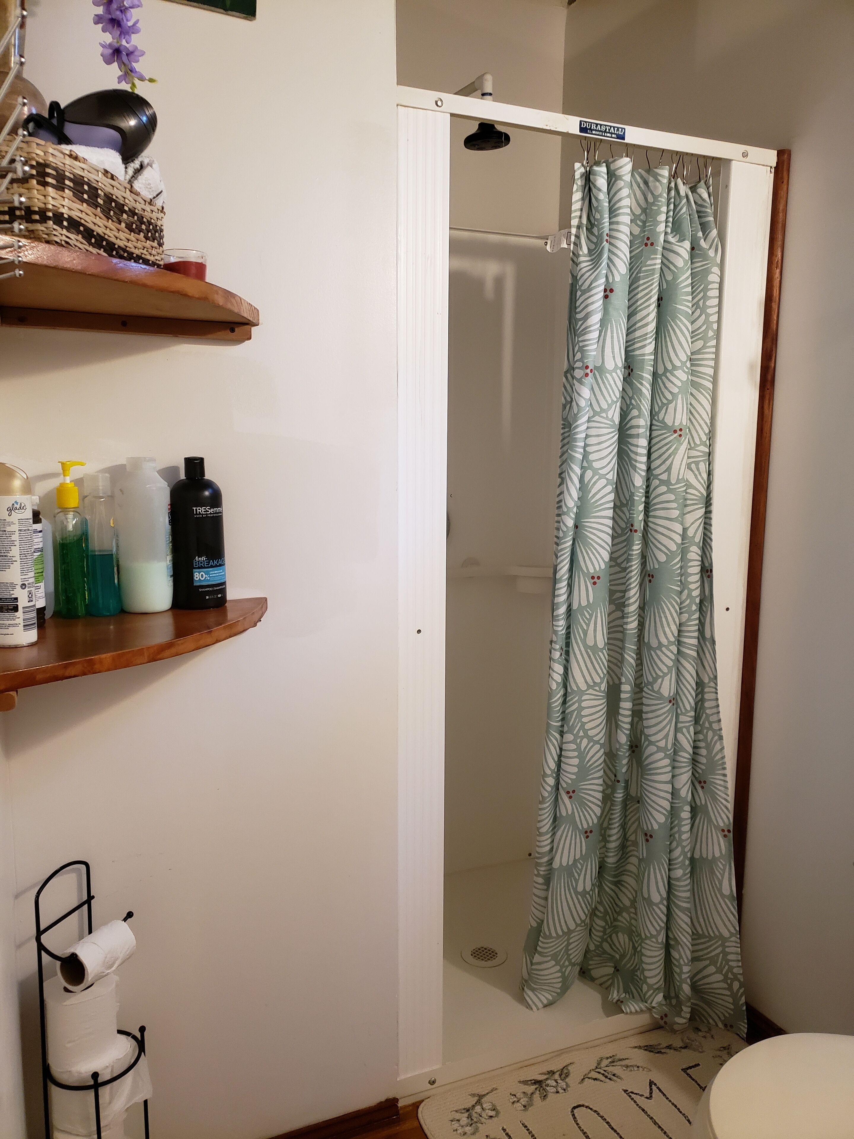 A bathroom with a shower curtain, shelves with toiletries, and a toilet paper holder.