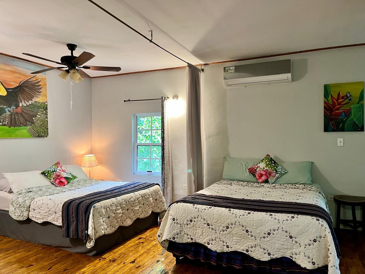 A room with two beds, a ceiling fan, a window with curtains, and a wall-mounted air conditioner.