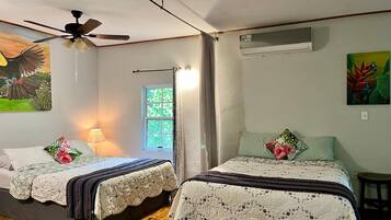 A room with two beds, a ceiling fan, a window with curtains, and a wall-mounted air conditioner.