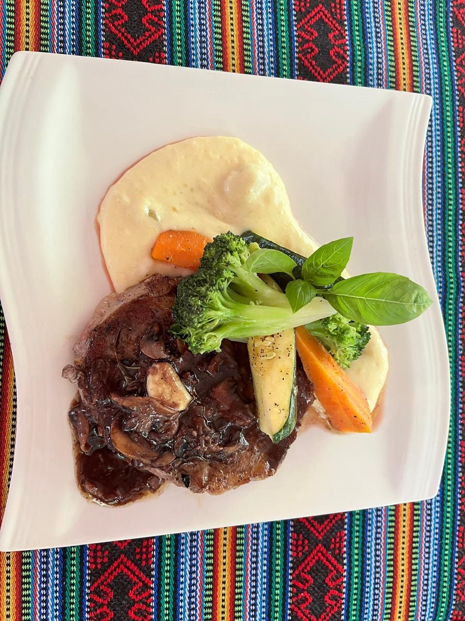 Un plato de comida con un guiso de carne, verduras y un acompañamiento cremoso.