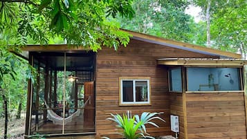 Una cabaña de madera con una hamaca, una ventana y una puerta.
