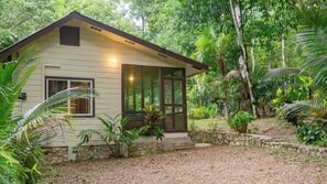Una pequeña casa de un solo piso con techo inclinado, rodeada de vegetación tropical densa.