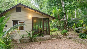 Una pequeña casa de un solo piso con techo inclinado, rodeada de vegetación tropical densa.