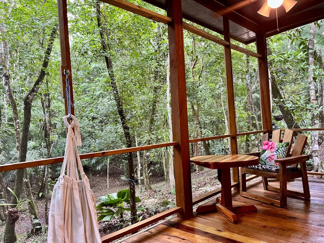 Una terraza de madera con una mesa y sillas, rodeada de un bosque denso.