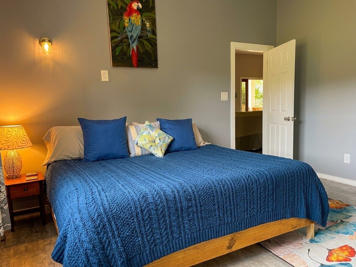 A bedroom with a bed, a nightstand, a lamp, a painting, and a door.