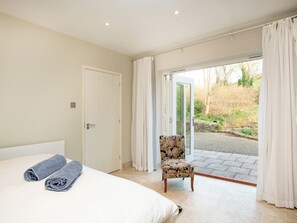 A bedroom with a bed, two rolled towels, a chair, and a sliding glass door leading to a garden. - The Studio at Granny's Well (Mixtow, near Fowey)