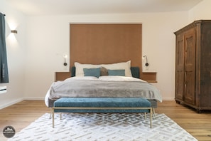 Ein Schlafzimmer mit Bett, einer Bank, einem Kleiderschrank und einer Wandleuchte.