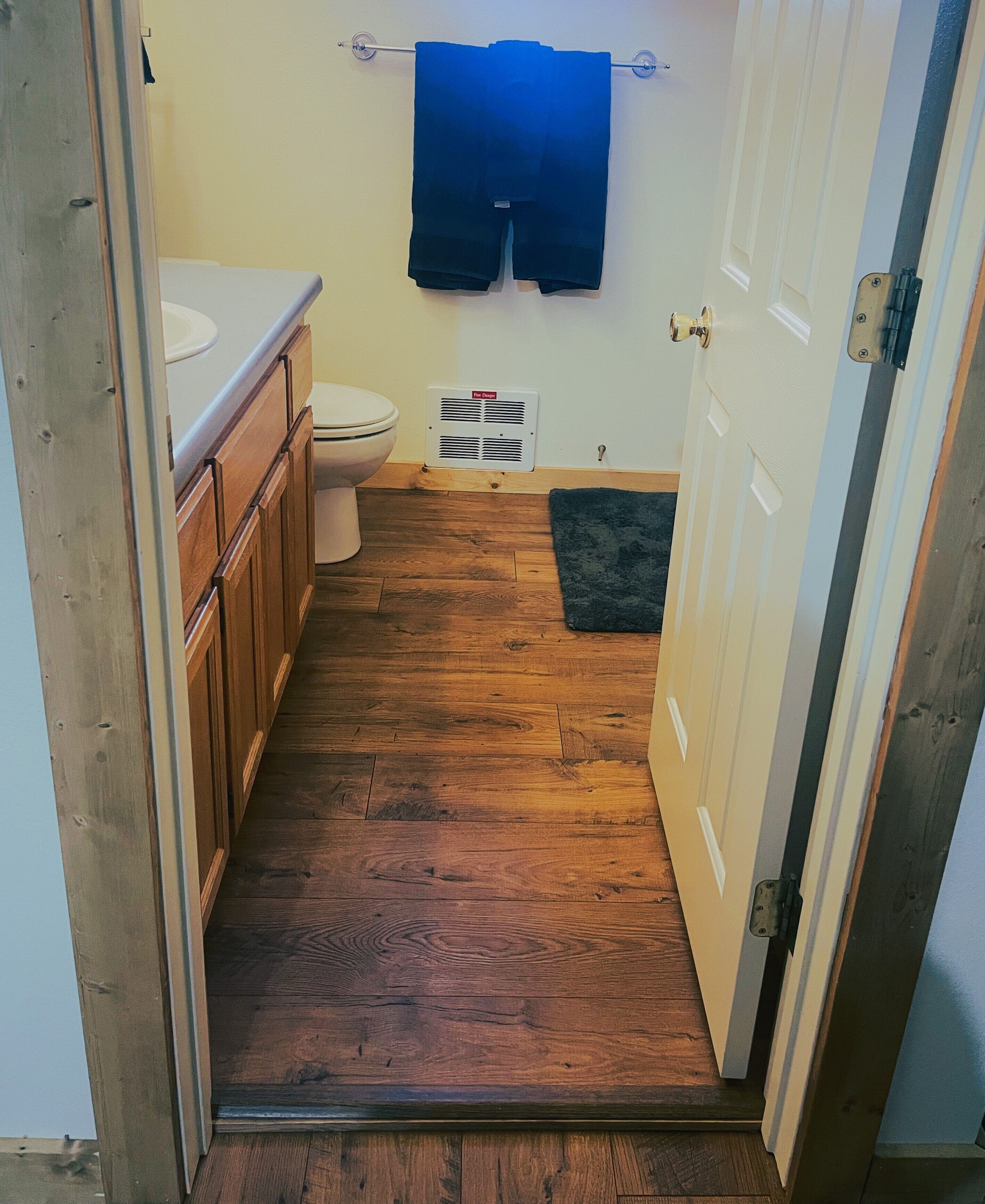 Een kleine badkamer met houten vloer, toilet, wastafel en handdoekhouder.