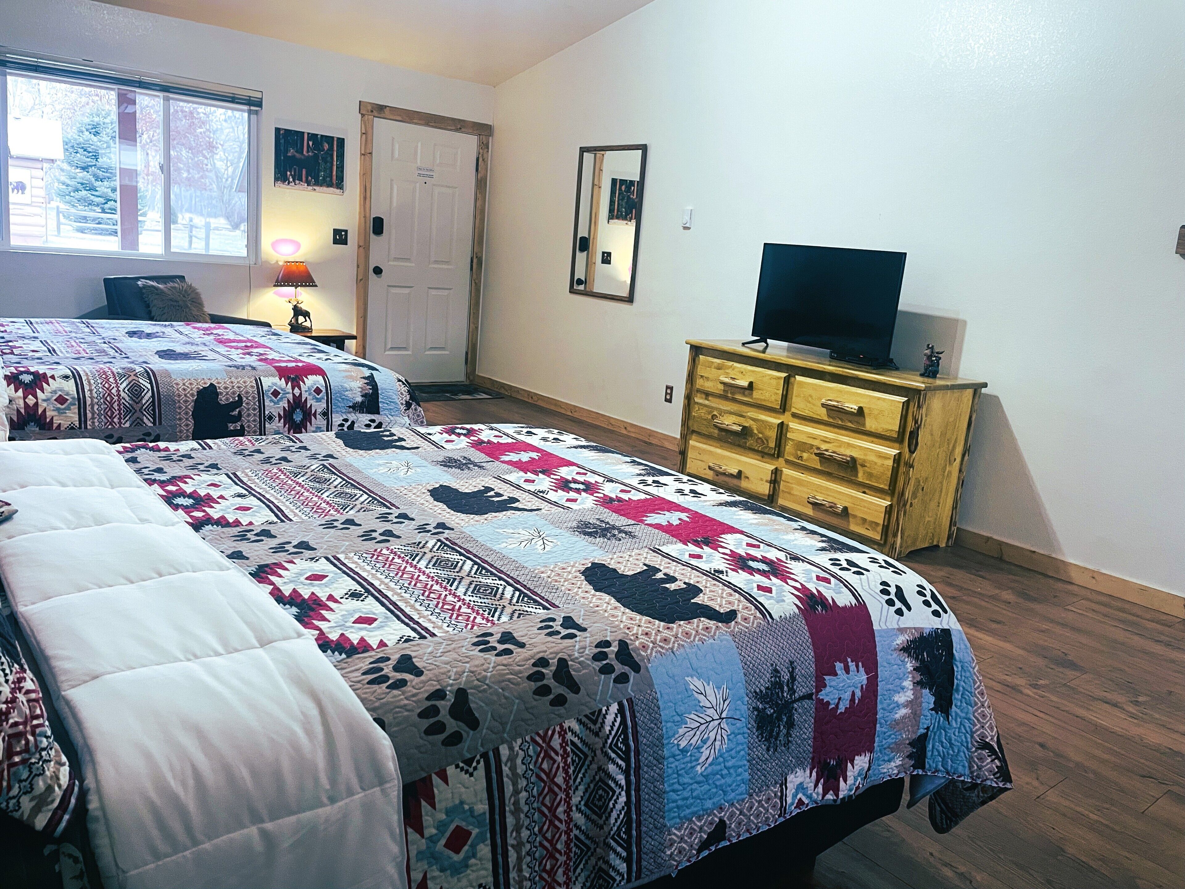 A bedroom with two beds, a dresser, a television, and a door.