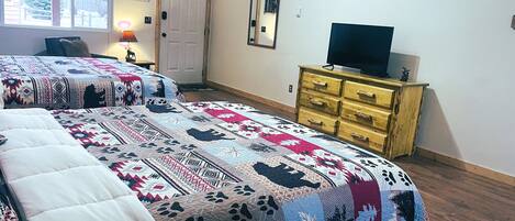 A bedroom with two beds, a dresser, a television, and a door.