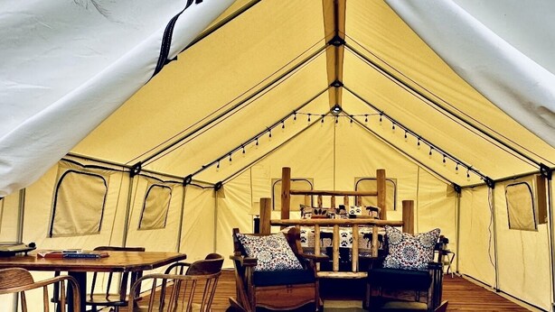 A tent with a wooden table and chairs, a sofa with patterned cushions, and a wooden bench.