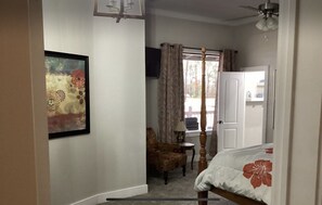 A bedroom with a bed, a chair, a desk, a window with curtains, and a painting on the wall.