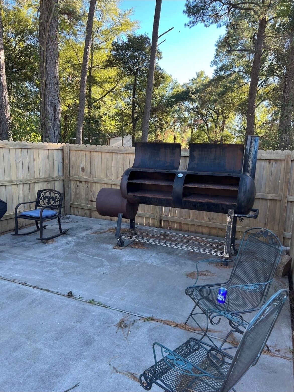 Un patio al aire libre con una parrilla de metal, dos sillas de metal y una valla de madera.
