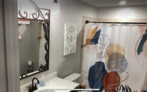 A bathroom with a white sink, black faucet, and a mirror with a decorative frame. There is a shower curtain with a colorful abstract design.