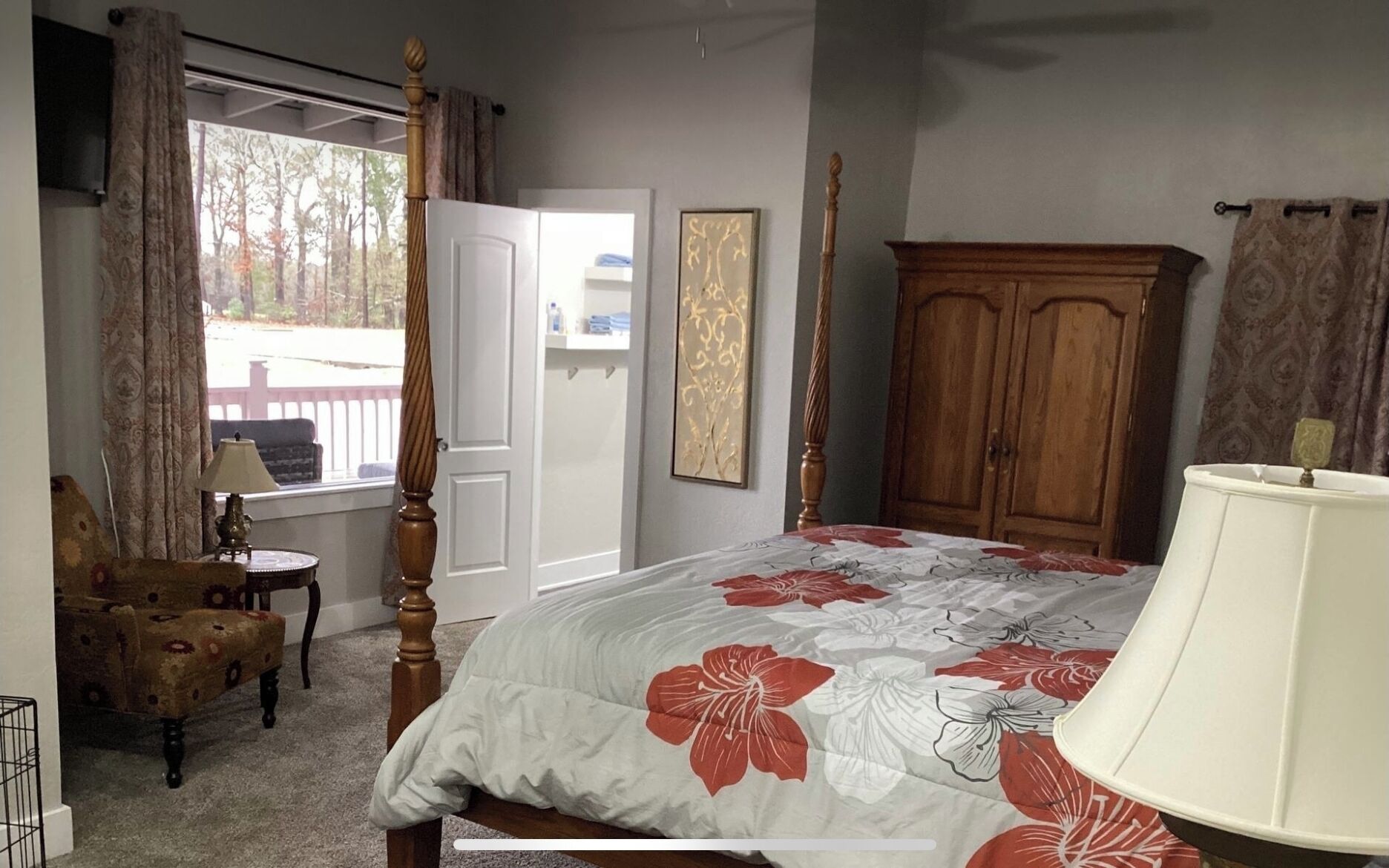 A bedroom with a four-poster bed, a wooden wardrobe, a chair, and a window with curtains.