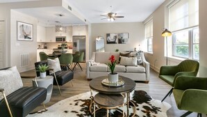 Ein geräumiges Wohnzimmer mit einer Couch, Sesseln, einem Couchtisch und einem Essbereich, im Hintergrund befindet sich eine Küche.