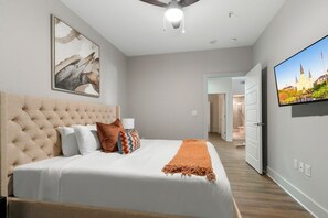 Een slaapkamer met een groot bed, een plafondventilator, een wandgemonteerde televisie en een deur naar een andere kamer.
