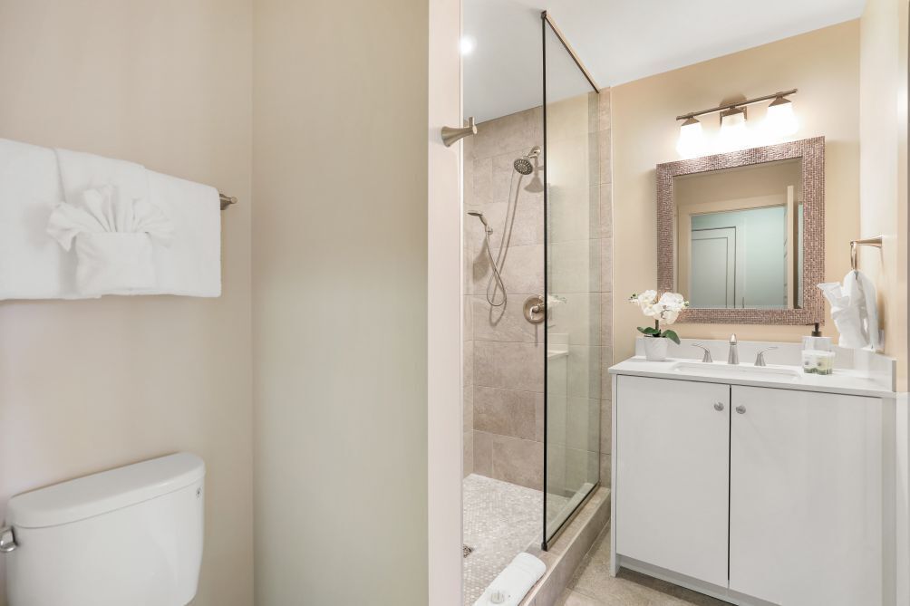 A modern bathroom with a glass-enclosed shower, a white sink with a mirror, and a toilet.