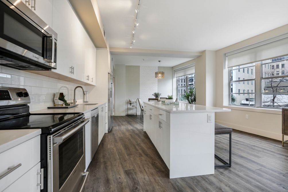A modern kitchen with white cabinetry, a central island, and a view of the city through large windows.