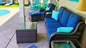 Een overdekt terras met rieten meubilair, een zwembad en plafondventilatoren.