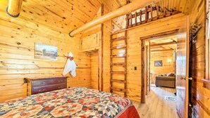 Interno di una baita in legno con un letto, una scala di legno e una porta che dà su un'altra stanza.