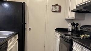 Una cocina con gabinetes blancos, un refrigerador negro, una estufa y un reloj en la pared.