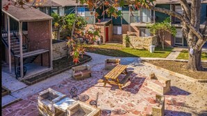 Un patio con mobiliario exterior, una fogata y una zona techada con escaleras.