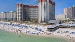 A beachfront hotel with multiple high-rise buildings, a sandy beach with numerous umbrellas, and a clear blue sky.