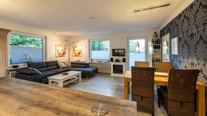Un salon moderne avec un canapé, une table à manger et des chaises. On y trouve une cheminée, un téléviseur et des œuvres d’art accrochées aux murs.