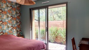 A bedroom with a bed, a sliding glass door to a patio, a wicker lamp, and a wall with a floral pattern. - 50 m from the lake, new wooden house - ideal family (Lacanau)