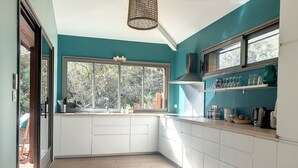 A modern kitchen with white cabinetry, a large window, and a teal accent wall. - 50 m from the lake, new wooden house - ideal family (Lacanau)