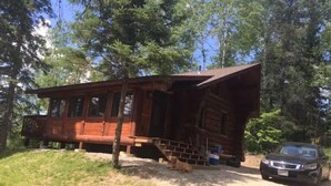 A wooden cabin with a porch, a dog lying on the ground, and a car parked nearby. - Cozy cottage trails, trout fishing & fireplace. (Marcell)