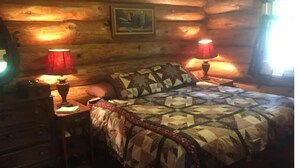 A cozy log cabin bedroom with a quilted bedspread, two bedside lamps, and a framed picture on the wall. - Cozy cottage trails, trout fishing & fireplace. (Marcell)