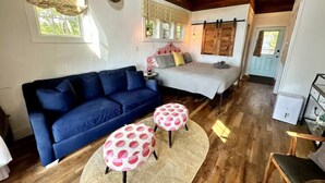 Una habitación acogedora con un sofá azul, una cama con ropa de cama estampada y dos otomanas redondas con lunares.