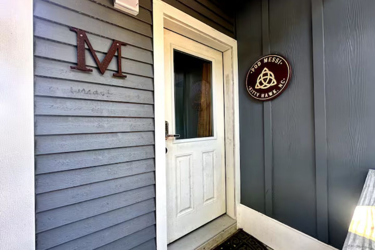 Une maison avec une porte blanche et un grand « M » peint sur le bardage.