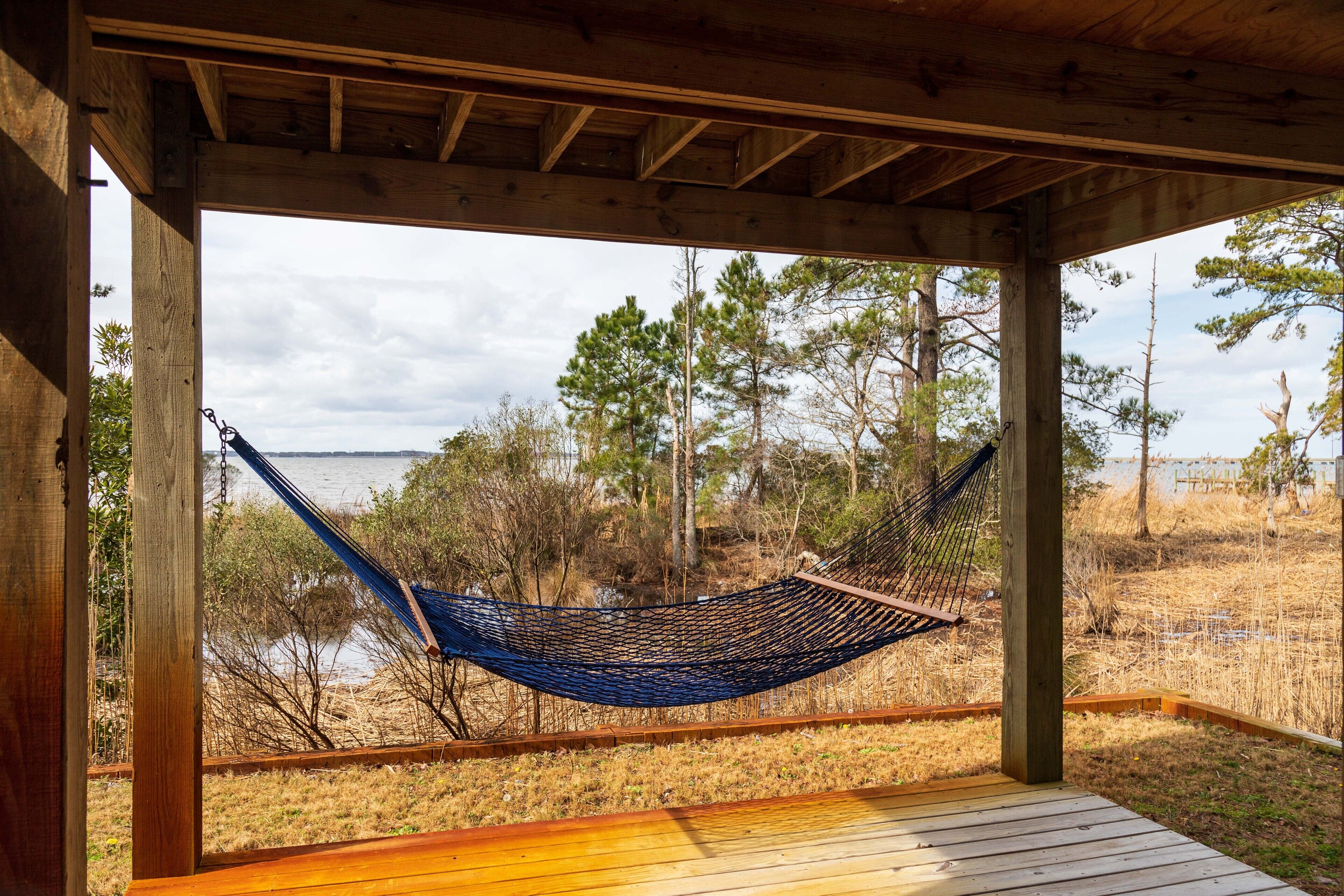 A hammock under a wooden structure with a view of a beach and trees.