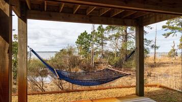 A hammock under a wooden structure with a view of a beach and trees.