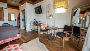 Una habitación acogedora con una cama, una mesita con sillas, un televisor y un espejo.