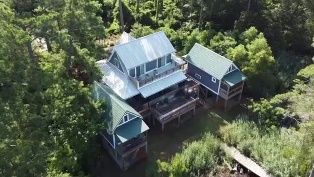 Una casa grande de varios pisos con techo de metal, rodeada por un bosque denso.