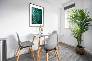 A modern dining area with a table, chairs, a framed artwork, a potted plant, and a window with a view.