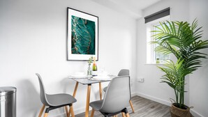 Ein stilvoller Essbereich mit Tisch, Stühlen, einem gerahmten Kunstwerk, einem Blumentopf und einem Fenster mit Aussicht.