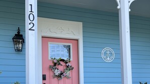 A porch with a pink door, a white chair, and a number 102 sign. - Cumberland Queen Cottage (St Marys)
